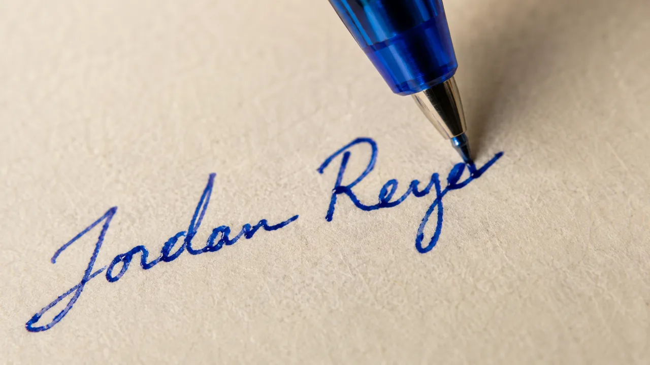 Close-up of a blue ballpoint pen writing the name Jordan Reyes in cursive on a cream envelope.